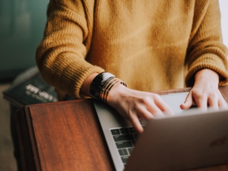 Frau sitzt an einem Tisch und tippt auf der Laptop-Tastatur