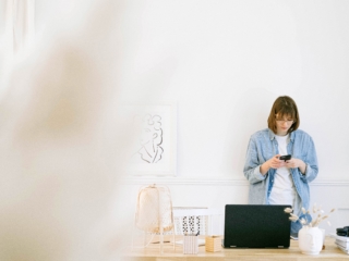 Frau mit Handy vor Laptop