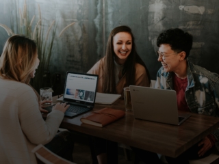 drei Personen sitzend und lachend mit Laptop