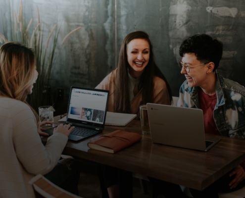 drei Personen sitzend und lachend mit Laptop